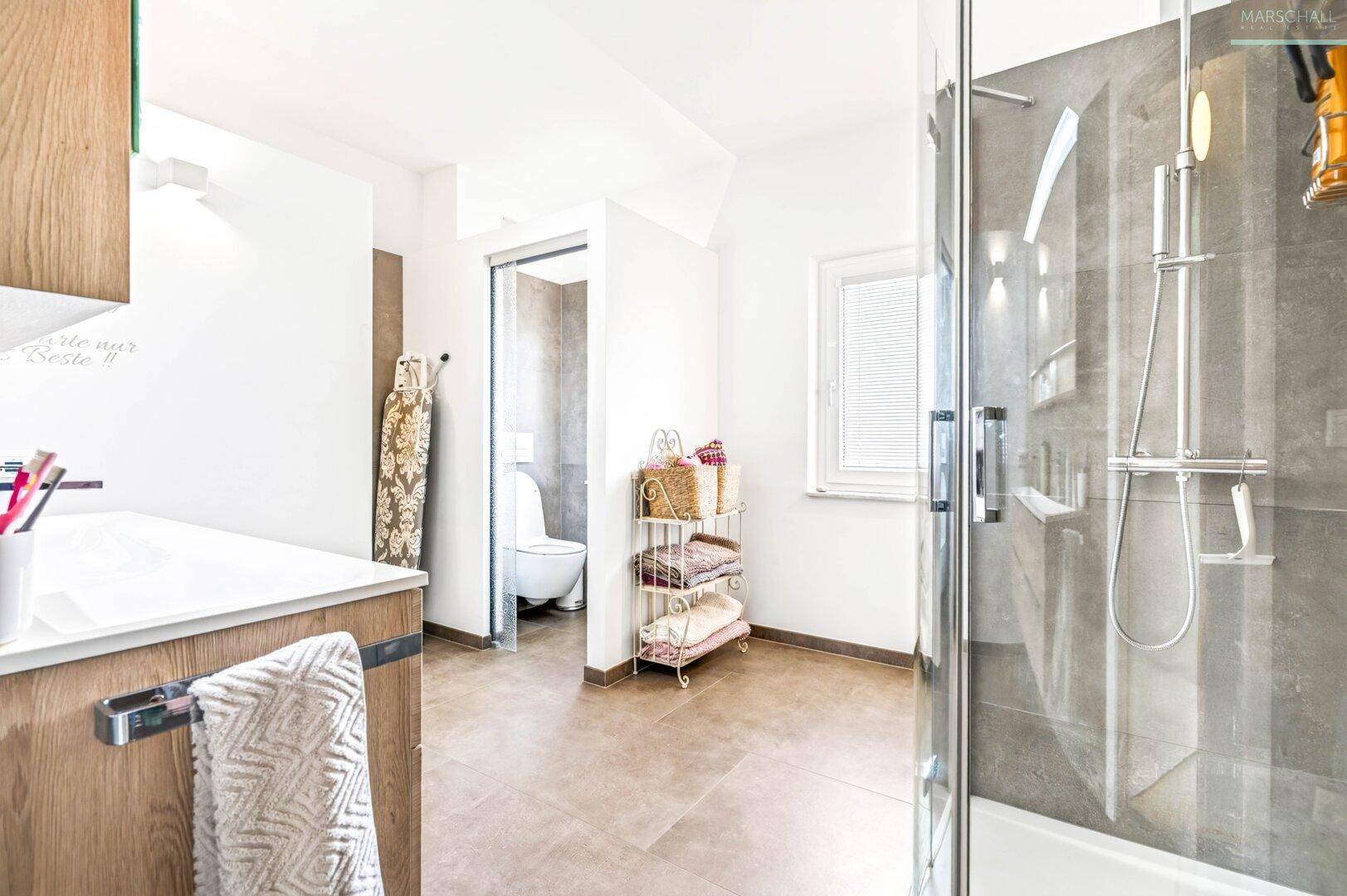 Helles Badezimmer mit Dusche, Fliesenboden und separatem WC-Bereich.