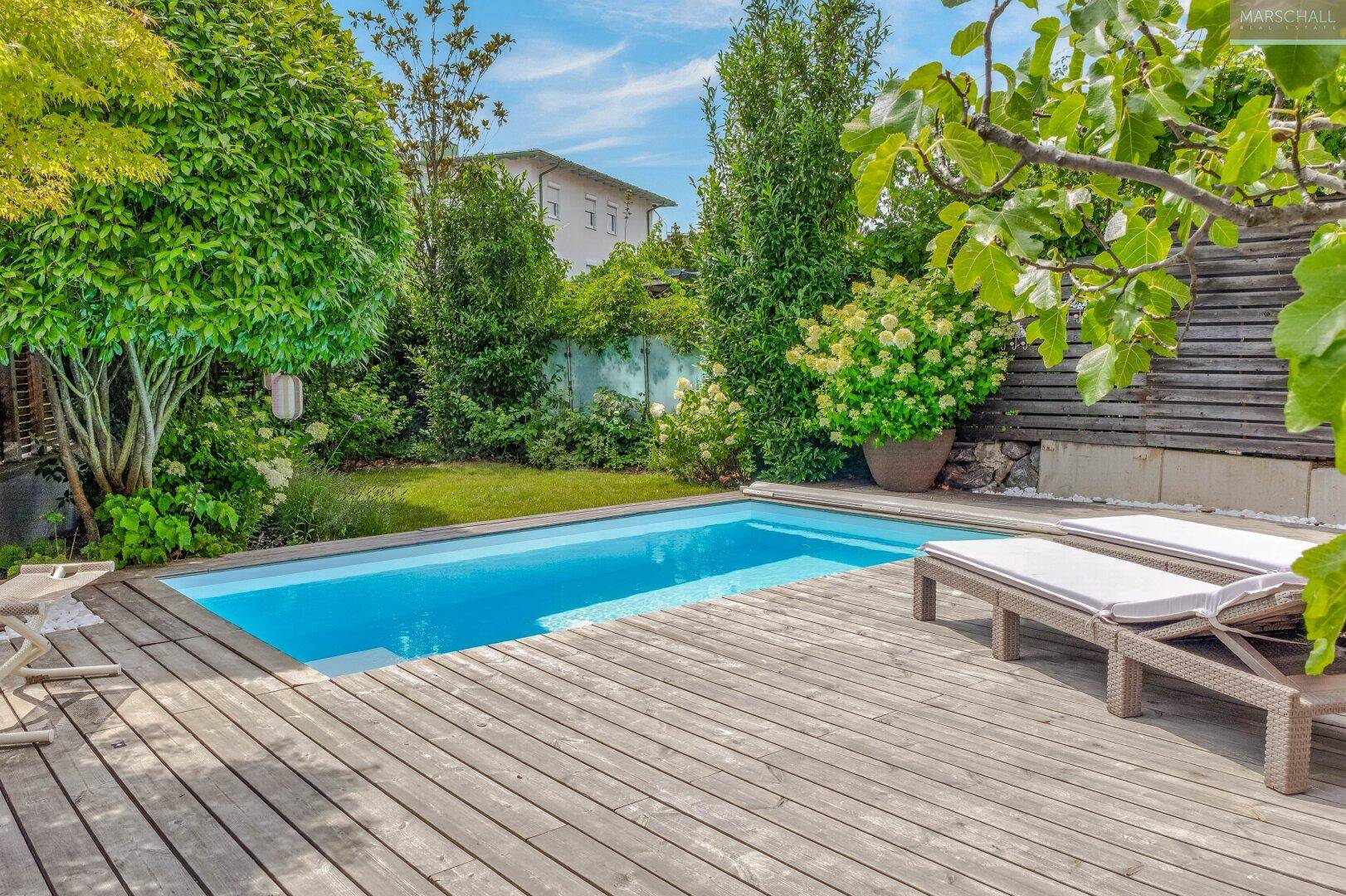 Gepflegter Garten mit Swimmingpool, Holzterrasse und üppiger Bepflanzung.