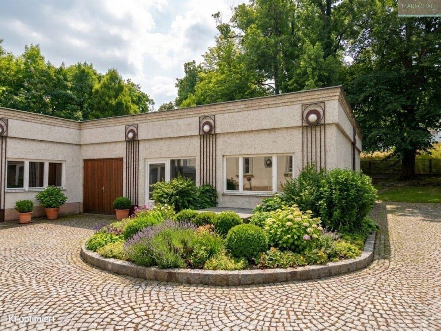 Nebengebäude mit gepflegtem Blumenbeet und gepflastertem Vorplatz, umgeben von Bäumen.