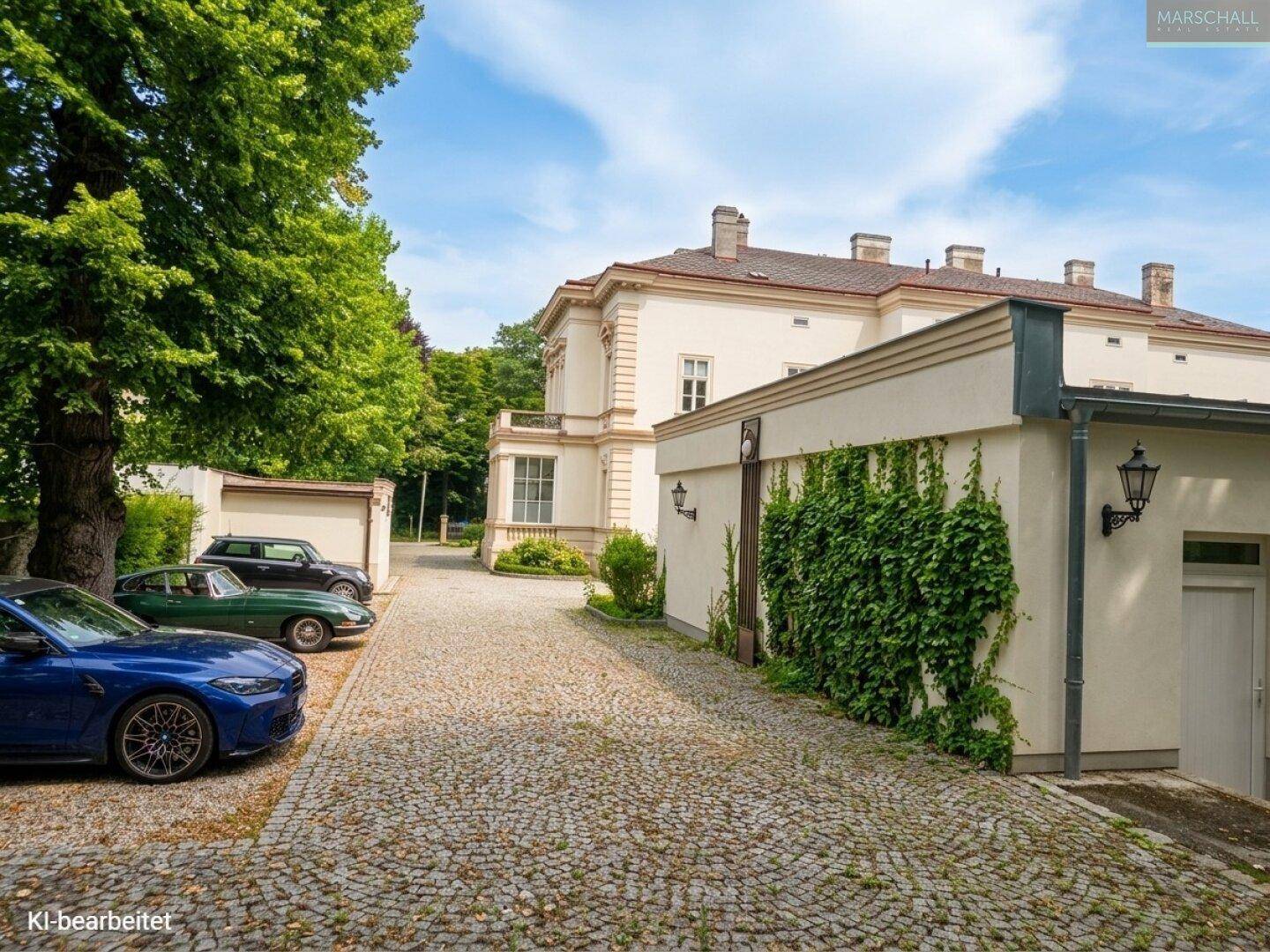 Historisches Anwesen mit gepflasterter Zufahrt, Garagen und geparkten Fahrzeugen.