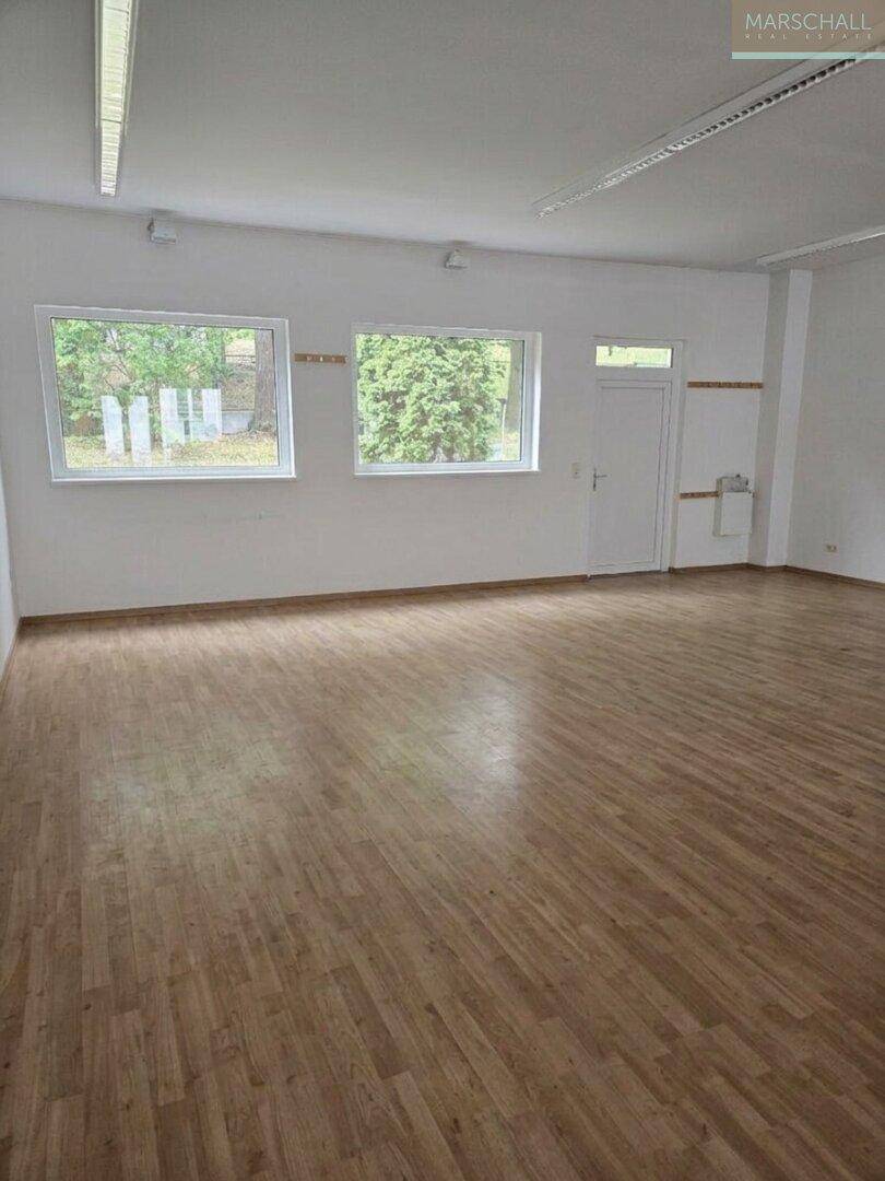 Geräumiger Raum mit Laminatboden und großen Fenstern, geeignet für verschiedene Nutzungen.