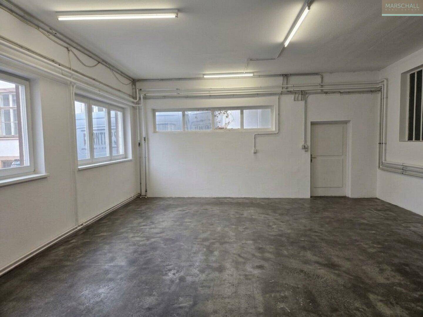 Funktionaler Raum mit Betonboden und Fenstern, ideal als Lager- oder Werkstattbereich.