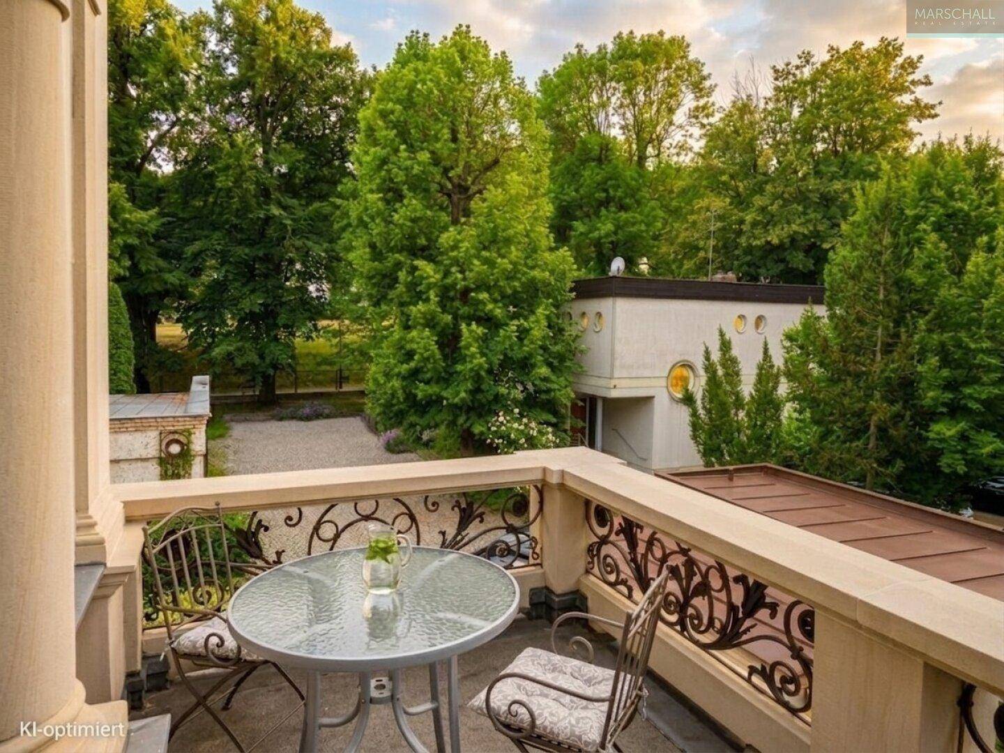 Romantischer Balkon mit schmiedeeisernem Geländer, Sitzgelegenheiten und Blick ins Grüne.