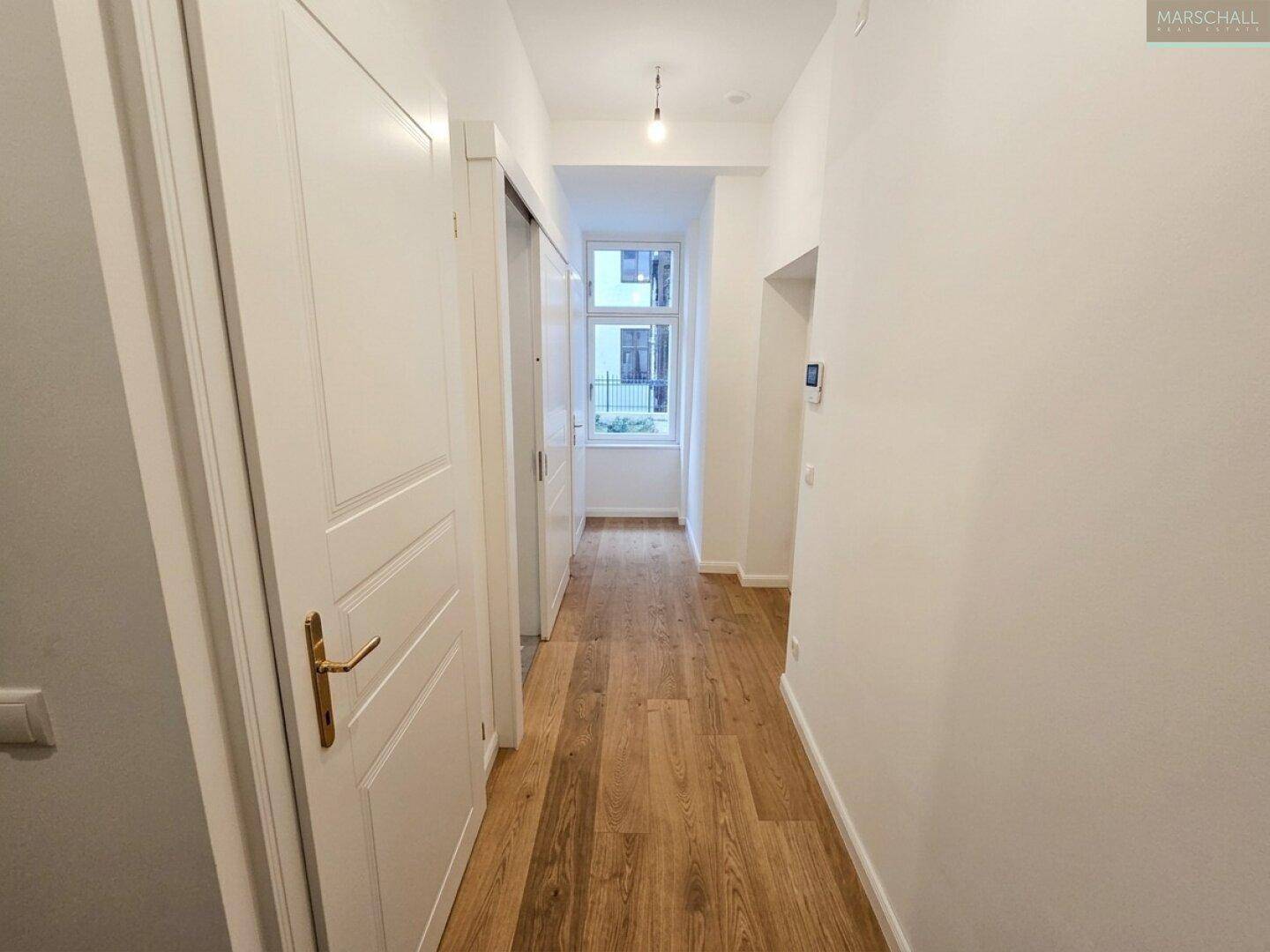 Langer, heller Flur mit Eichenparkettboden und einem Fenster am Ende, das Tageslicht hereinlässt.