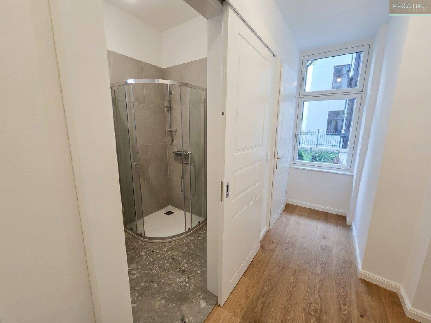 Modernes Badezimmer mit Duschkabine und grauen Fliesen, durch Schiebetür zugänglich.