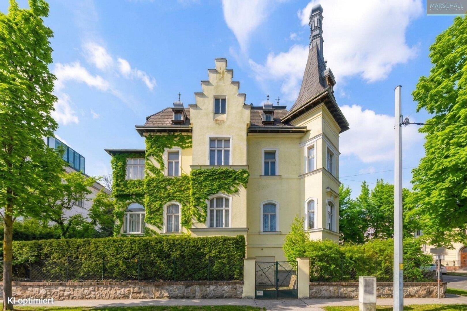 Historische Villa mit Efeubewuchs und markantem Giebel, umgeben von einer Hecke.