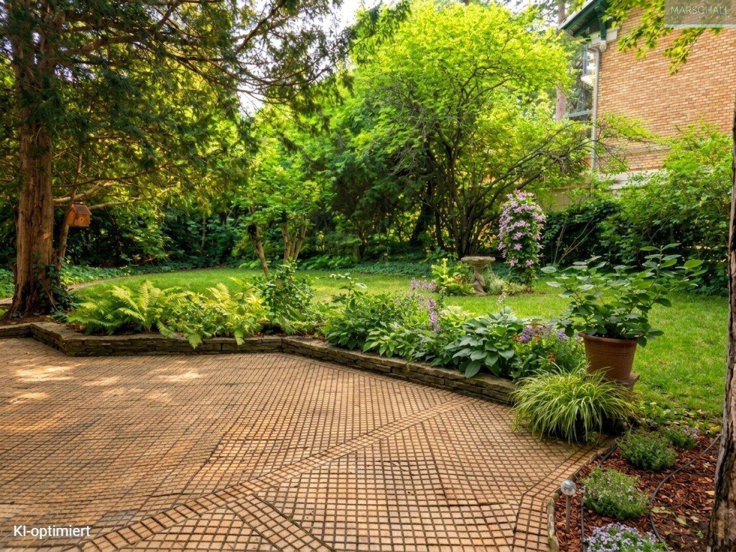 Geräumige Terrasse mit dekorativem Fliesenmuster, umgeben von üppigem Grün und Bäumen.