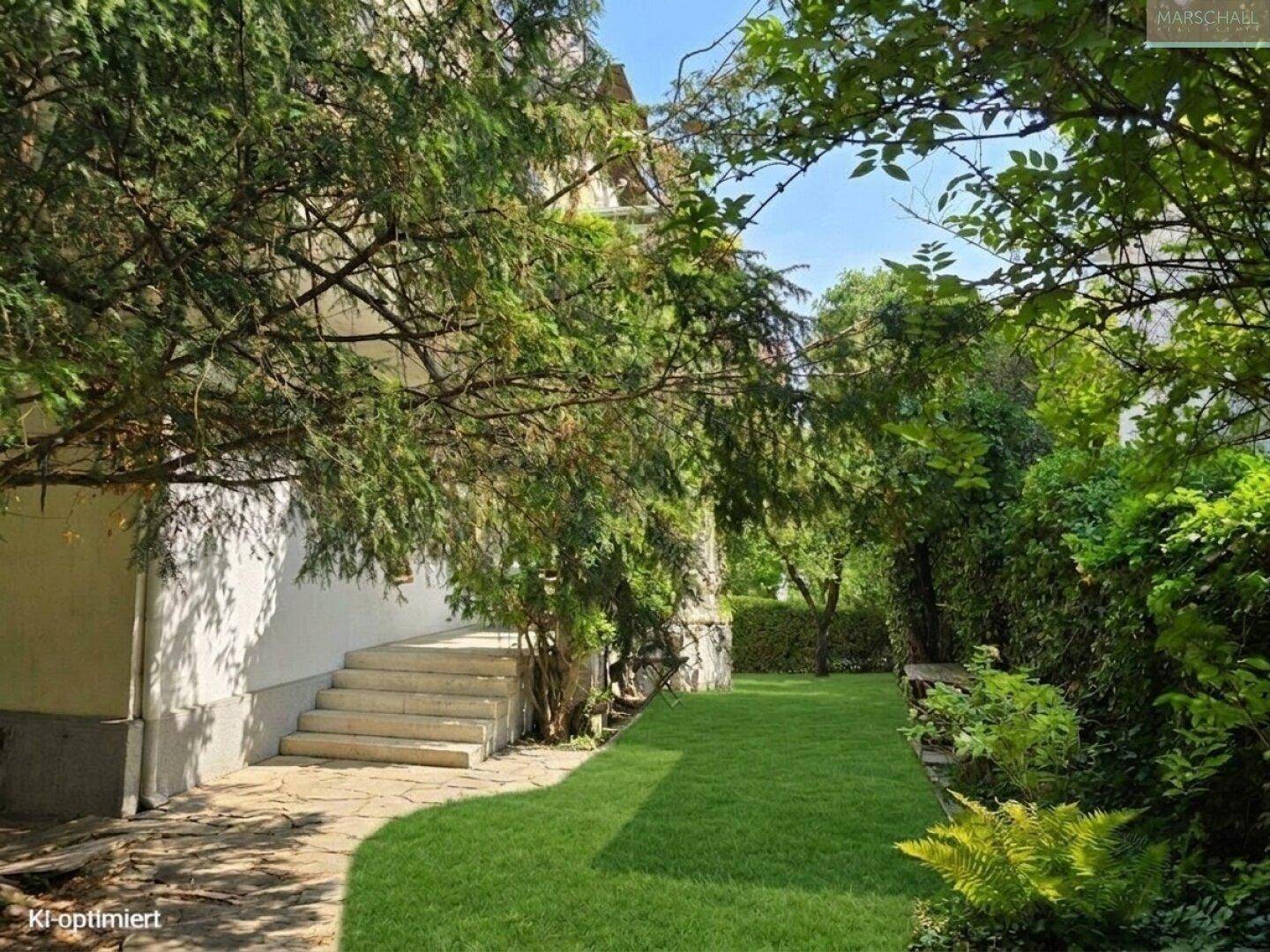 Grüner Gartenbereich mit Rasen und Steinweg, umgeben von Bäumen und Sträuchern.