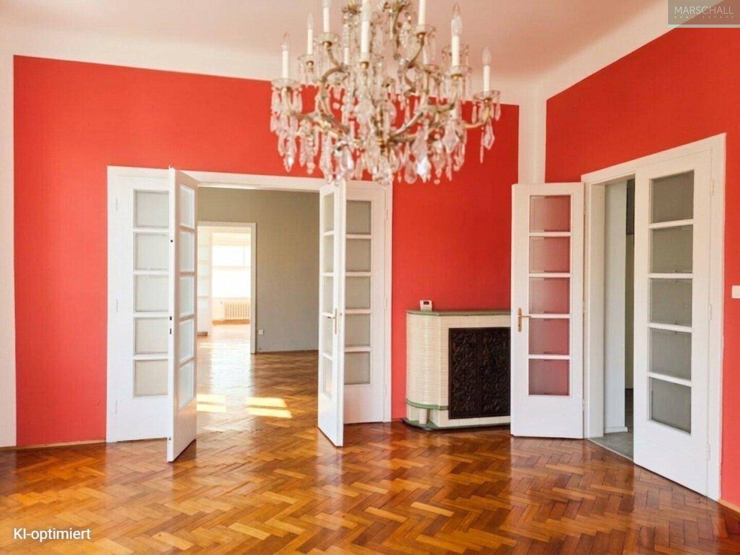 Geräumiges Wohnzimmer mit Fischgrätparkett, roter Wandfarbe und Kronleuchter.
