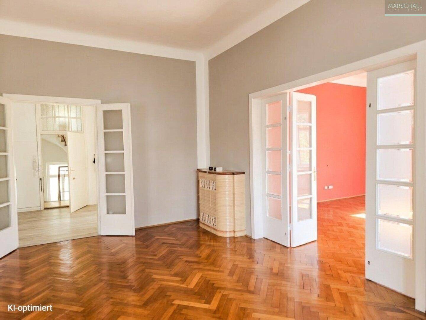 Helles Wohnzimmer mit Fischgrätparkett, grauen Wänden und Zugang zu weiteren Räumen.