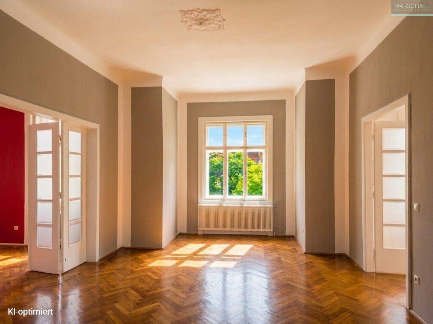 Großes Wohnzimmer mit Fischgrätparkett, grauen Wänden und viel Tageslicht.