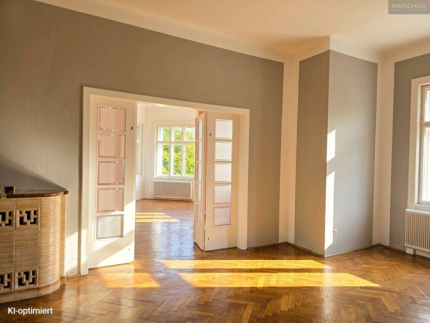 Helles Wohnzimmer mit Fischgrätparkett, grauen Wänden und sonnigem Ambiente.