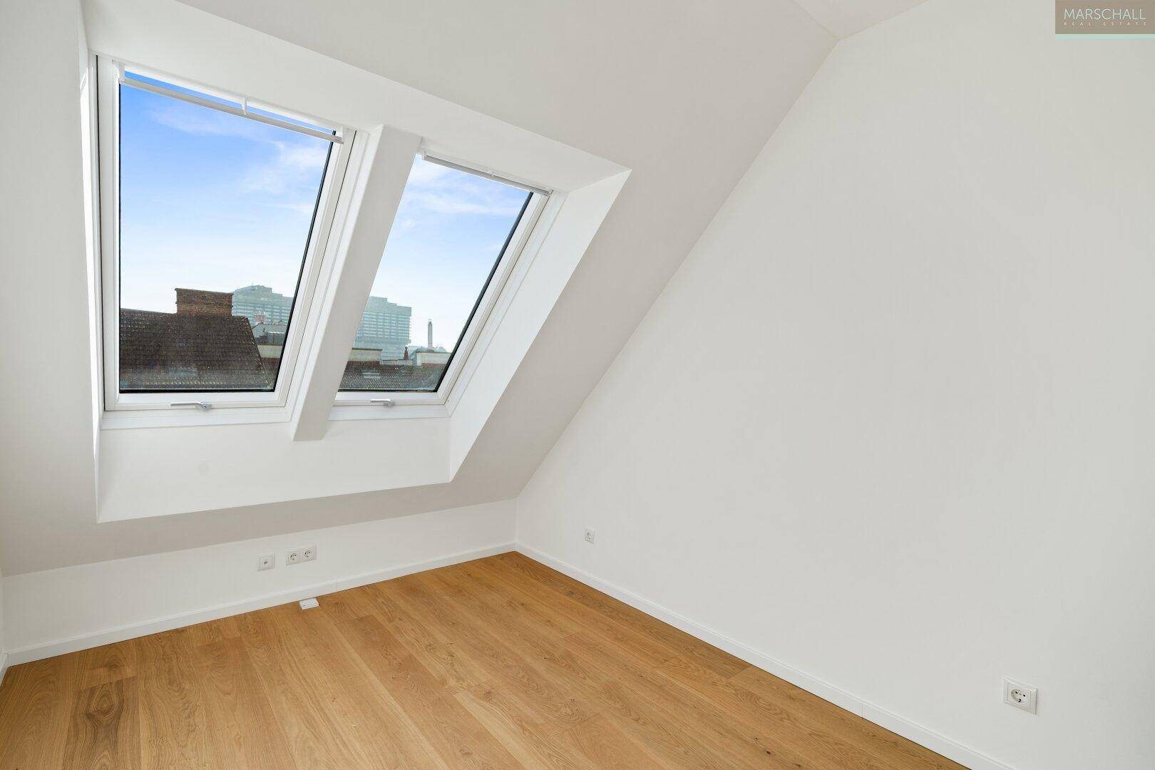 Geräumiger Raum mit Holzboden und schrägen Dachfenstern, ideal für ein Schlafzimmer oder Büro.