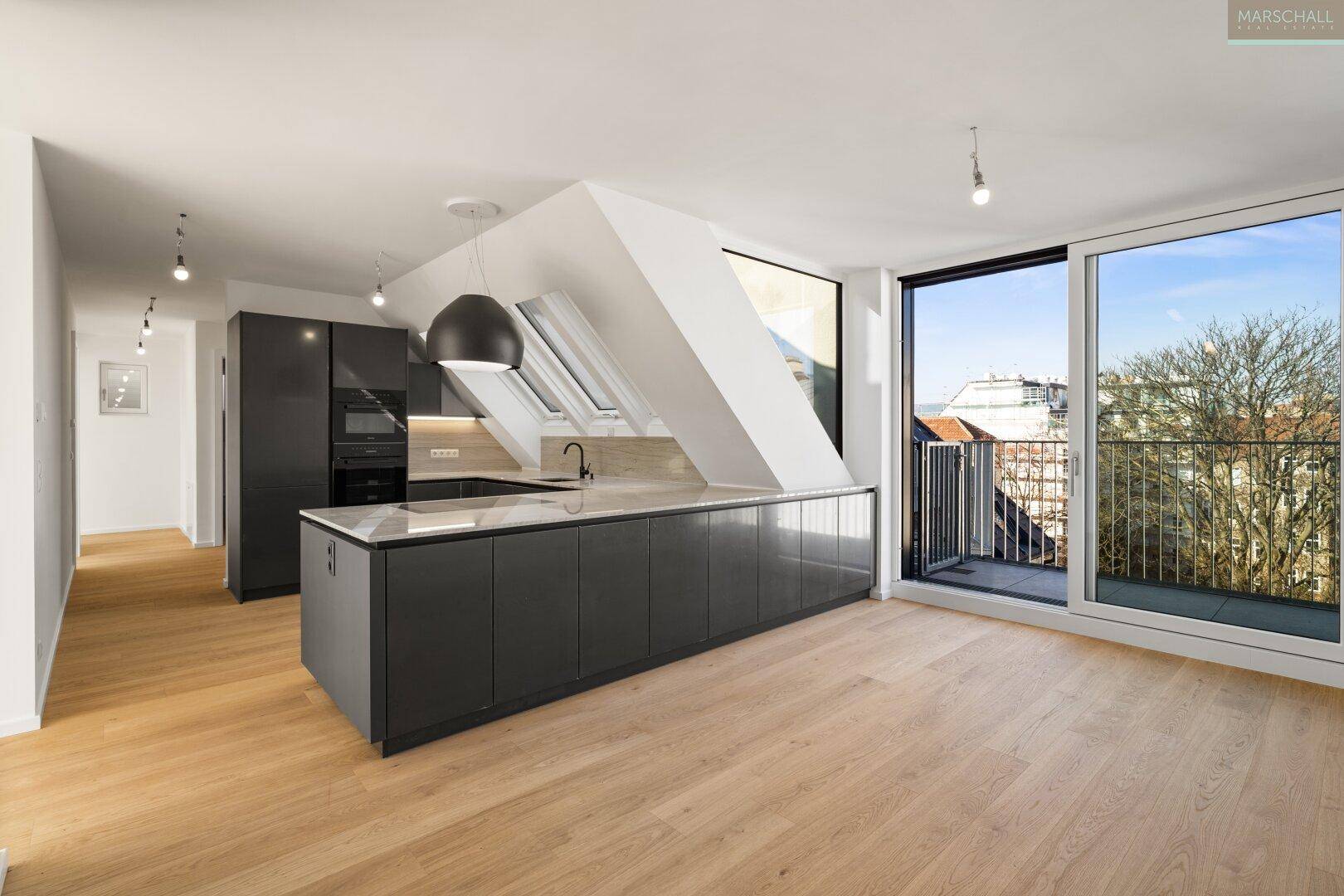 Offener Wohnbereich mit moderner grauer Küche, Holzboden und Zugang zu einem Balkon.