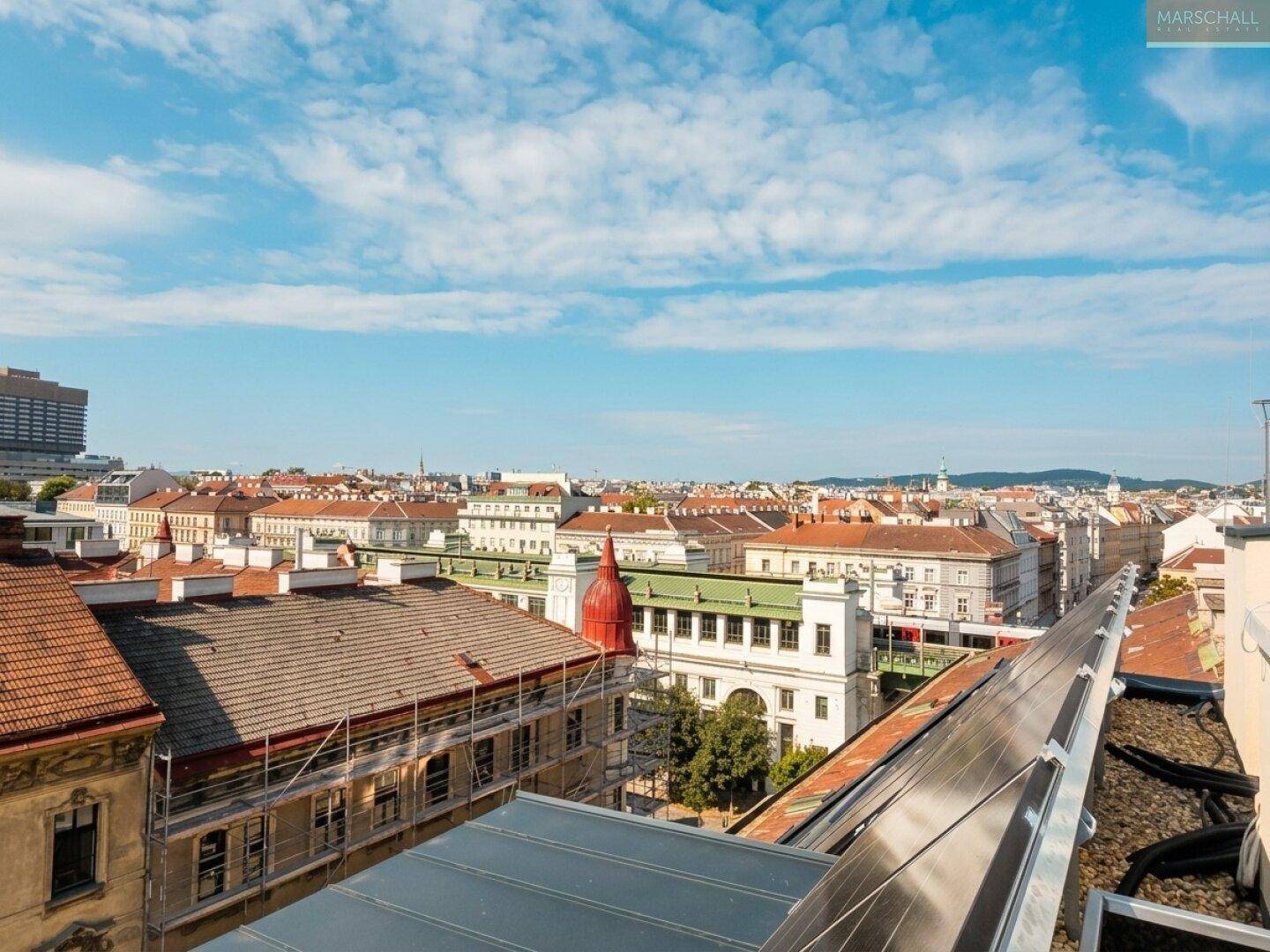 Ausblick über die Dächer der Stadt mit Baugerüsten und Solaranlagen im Vordergrund unter blauem Himmel.