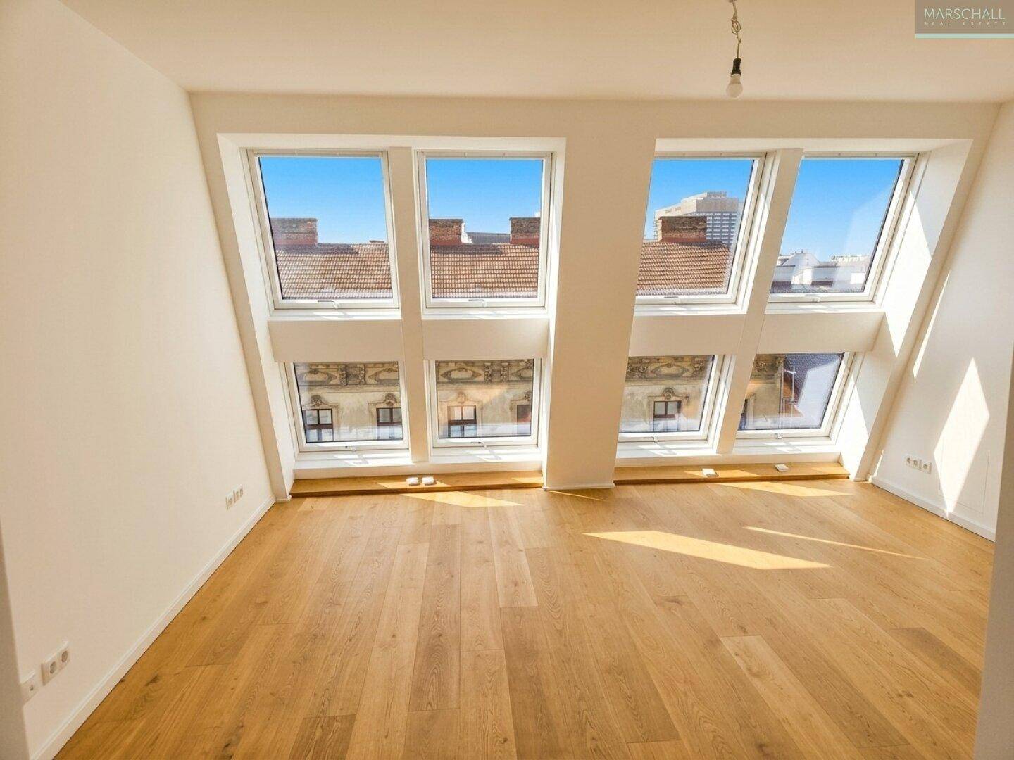 Heller Raum im Dachgeschoss mit Holzboden und großen Dachfenstern, die viel Licht hereinlassen.