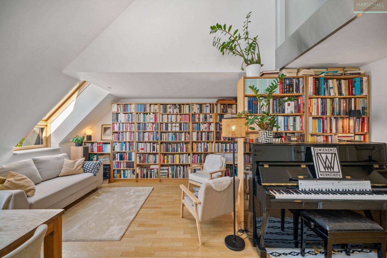 Gemütliches Wohnzimmer mit Dachschrägen, einem Klavier, raumhohen Bücherregalen und viel natürlichem Licht.