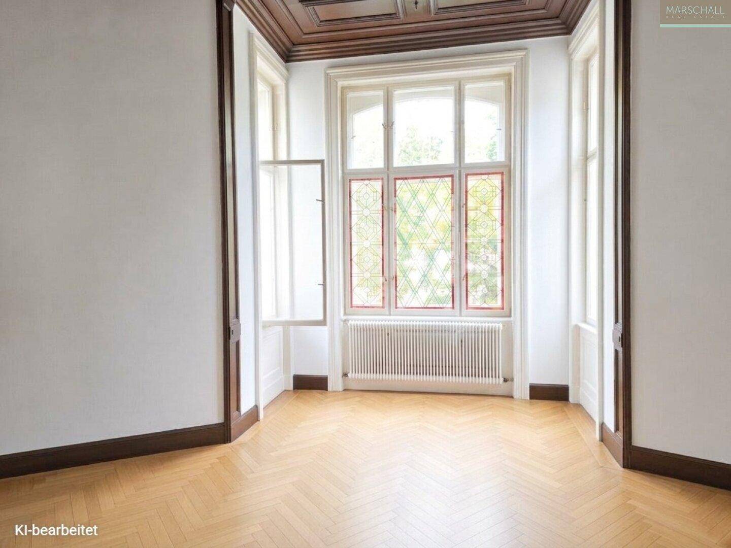 Heller Raum mit Fischgrätparkett und großen Erkerfenstern, die mit dekorativem Buntglas verziert sind.