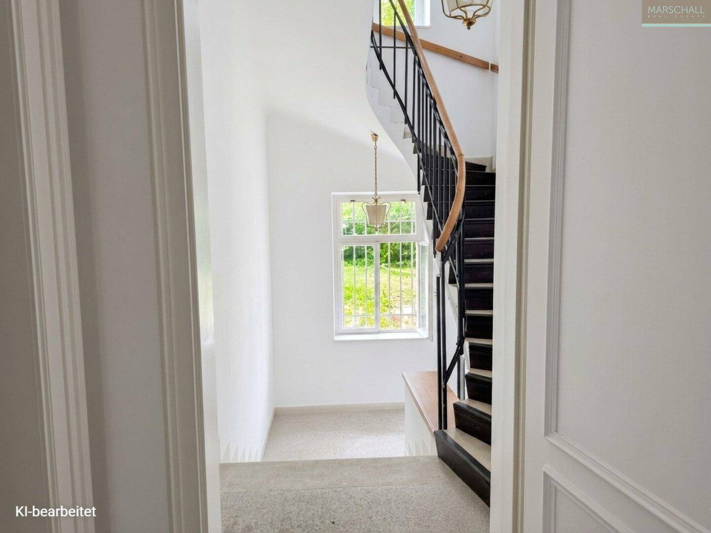 Elegantes Treppenhaus mit geschwungener Holztreppe und großem Fenster, das viel Tageslicht hereinlässt.