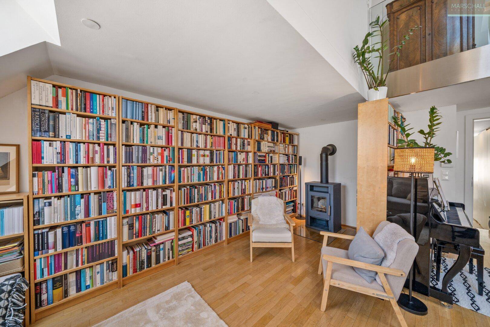 Geräumiges Wohnzimmer mit großer Bücherwand, zwei Sesseln und einem modernen Holzofen für gemütliche Abende.