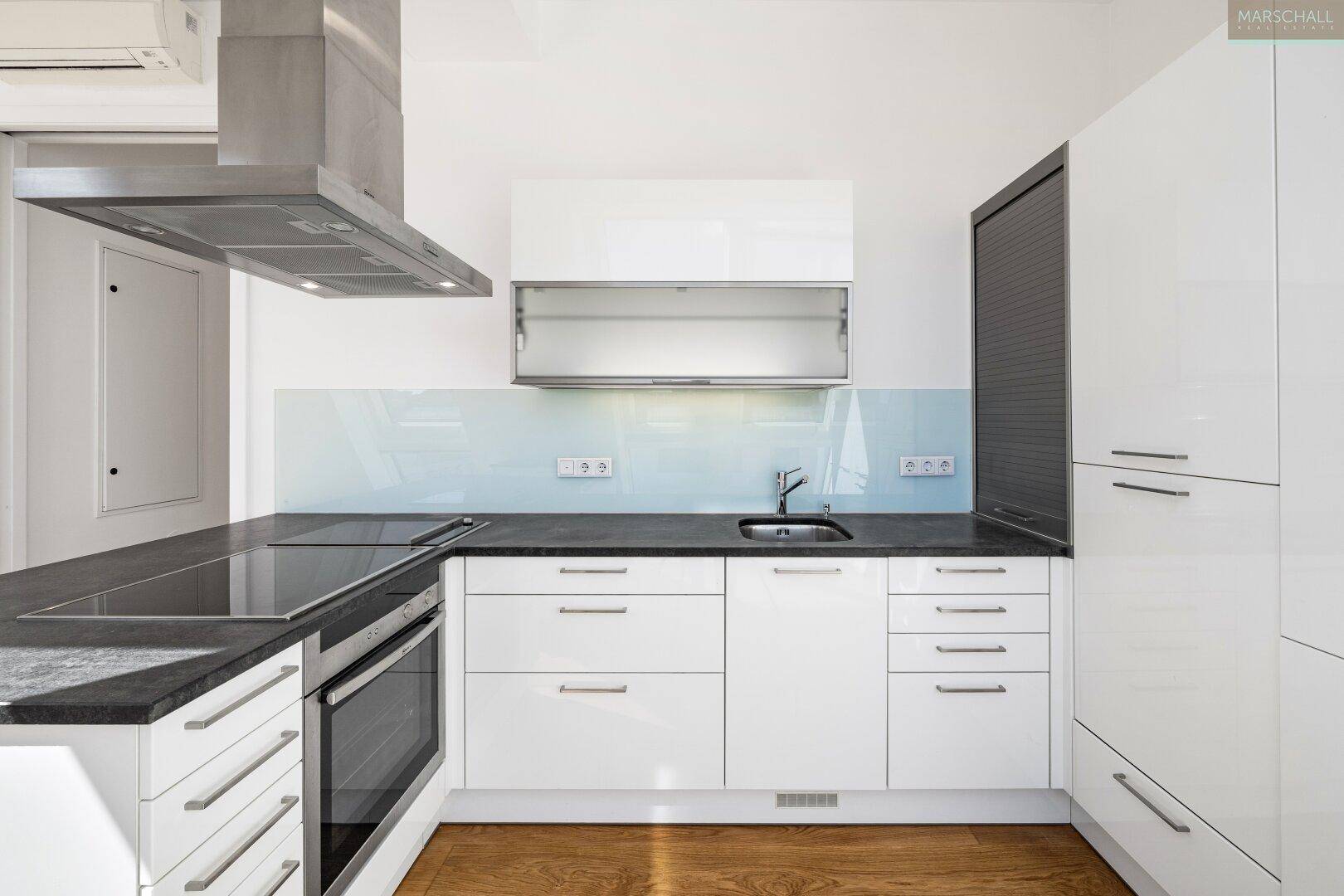 Moderne weiße Einbauküche mit dunkler Arbeitsplatte, Induktionskochfeld und Dunstabzugshaube.