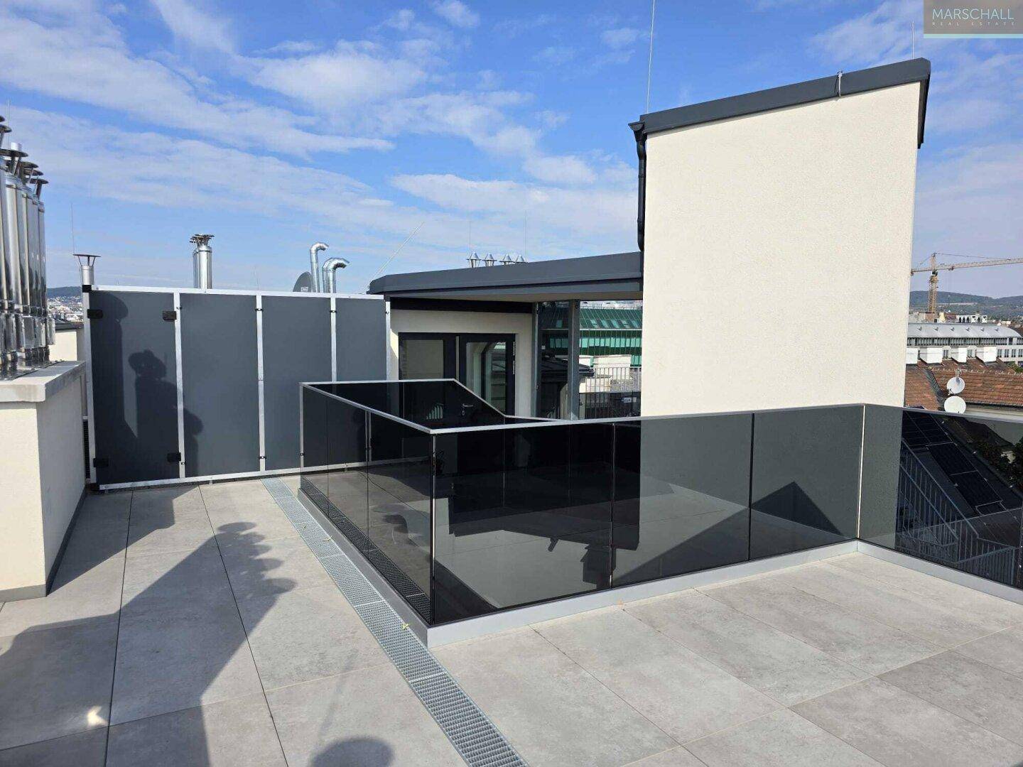 Moderne Dachterrasse mit Glasgeländer und Fliesenboden bietet einen weiten Blick über die Stadt.