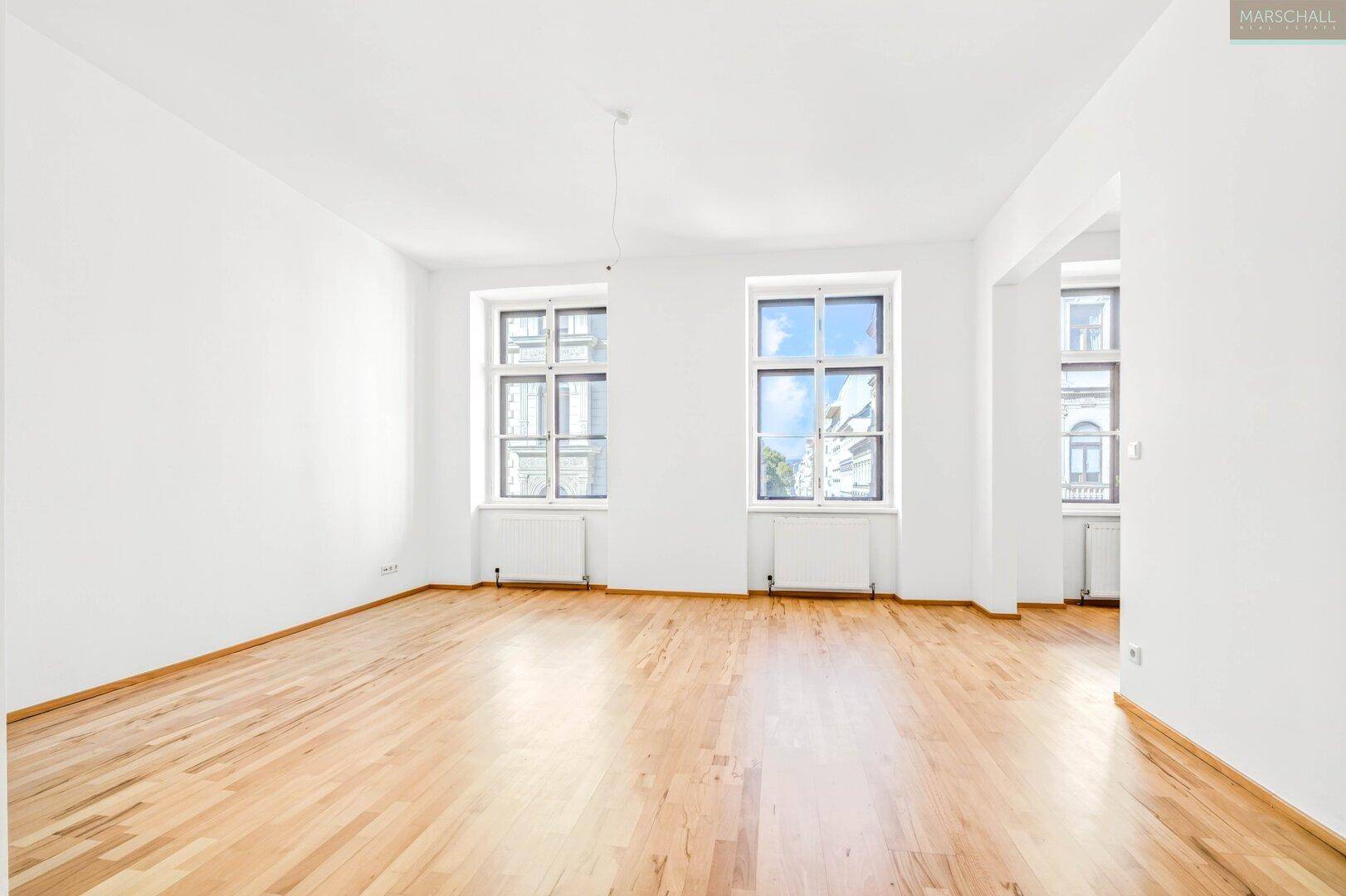 Geräumiger, heller Raum mit Holzboden und großen Fenstern, ideal für Wohnzwecke.