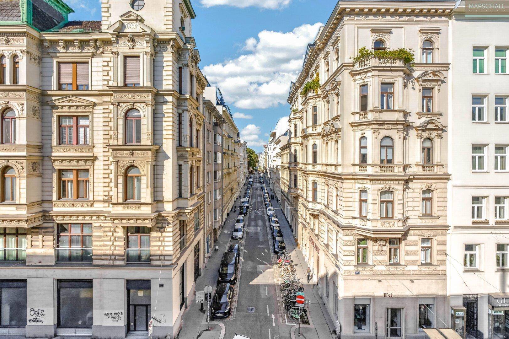 Historische Straße mit beeindruckenden Gebäudefassaden und parkenden Autos.