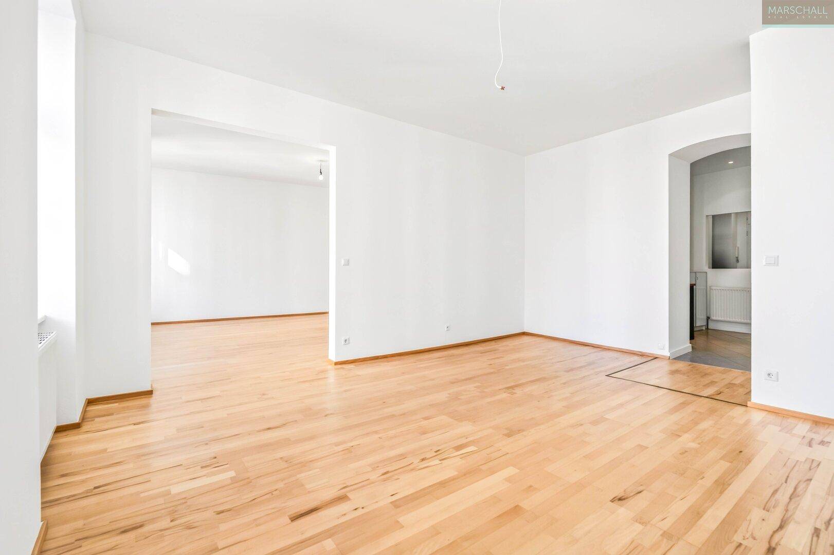 Heller Raum mit Holzboden und elegantem Bogenzugang zu weiteren Zimmern.