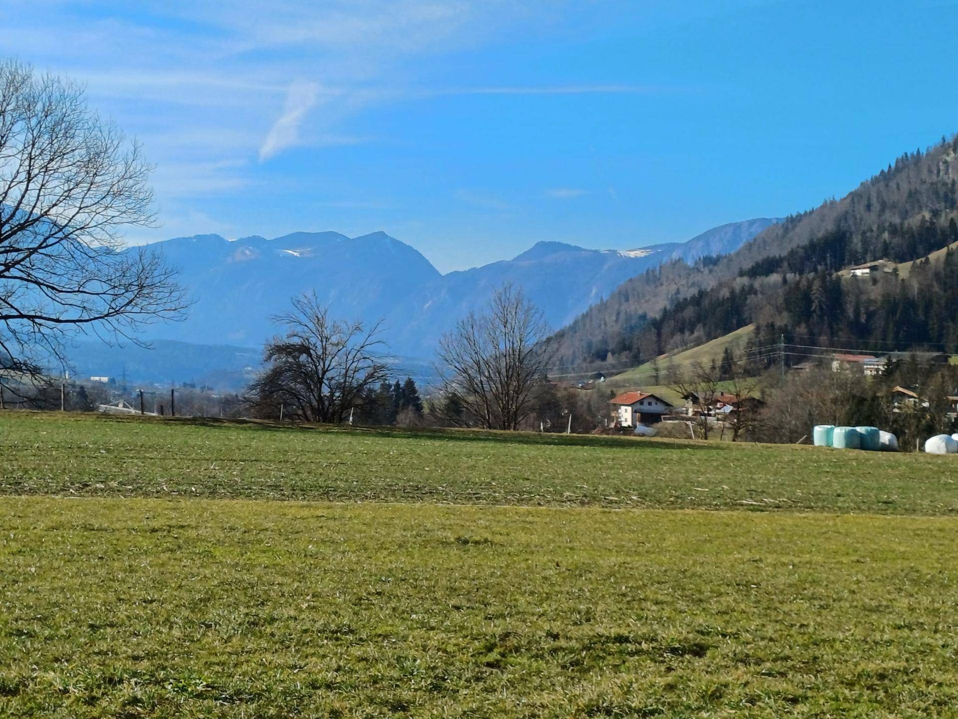 Weitläufige grüne Wiesen mit Blick auf die majestätischen Berge und vereinzelte Häuser in der Ferne.