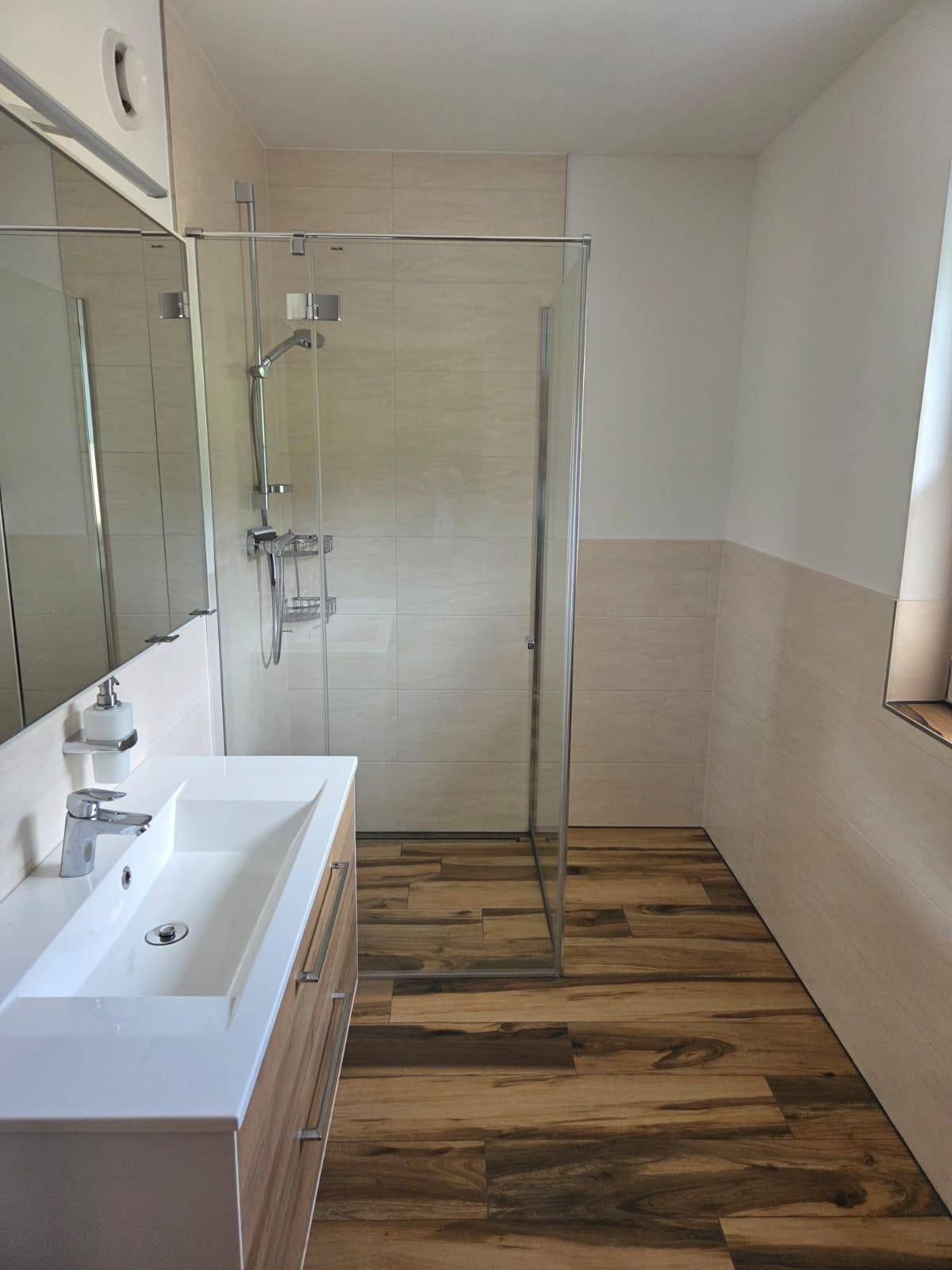 Helles Badezimmer mit begehbarer Dusche, Einzelwaschbecken und Holzoptikboden.