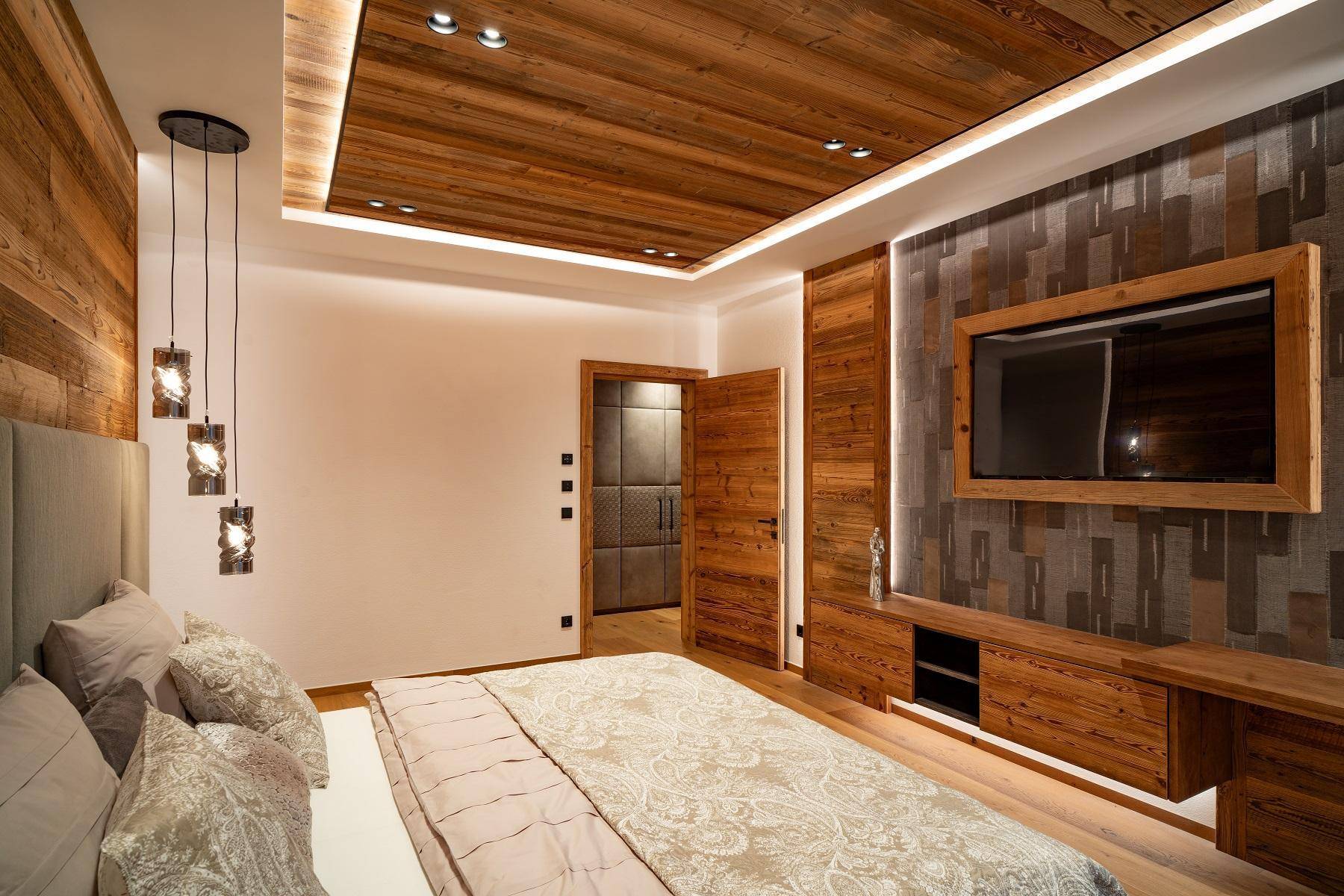 Modernes Schlafzimmer mit Holzwand, integriertem Fernseher und indirekter Beleuchtung.