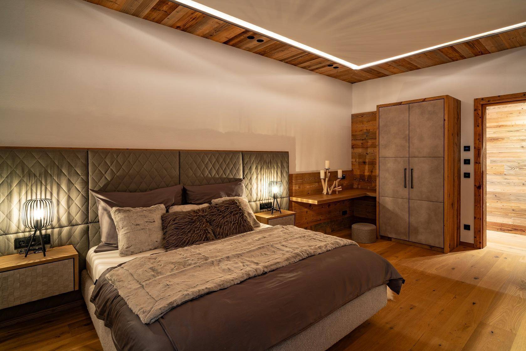 Gemütliches Schlafzimmer mit Holzboden, Holzbalkendecke und indirekter Beleuchtung.