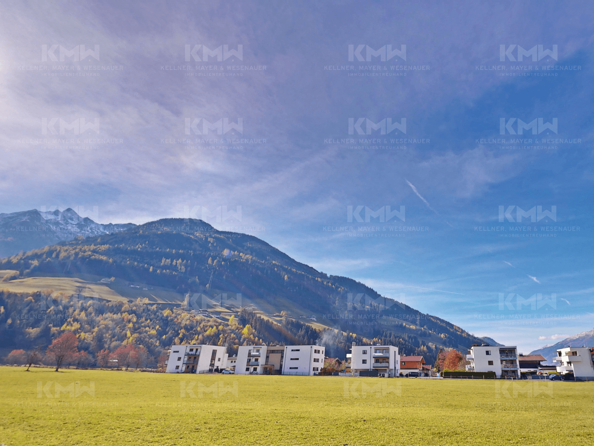 Panoramablick auf die umliegende Berglandschaft und grüne Wiesen unter blauem Himmel.
