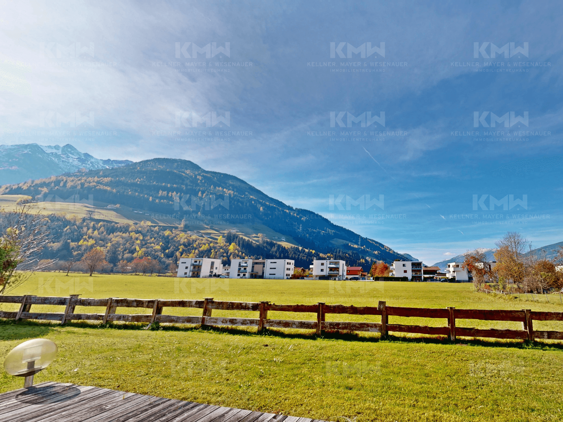 Weitläufige grüne Landschaft mit Blick auf die Berge und moderne Gebäude in der Ferne.