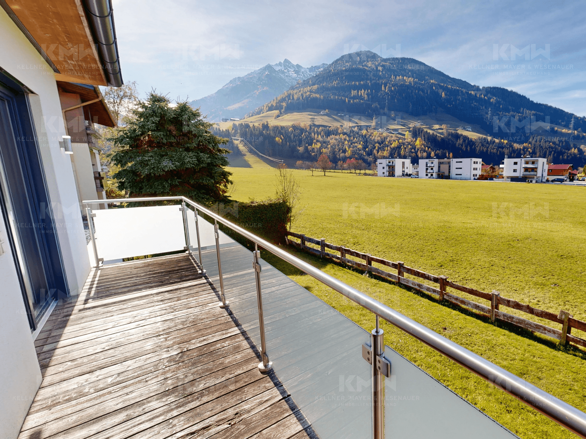 Geräumiger Balkon mit Holzboden und atemberaubendem Blick auf die umliegende Bergwelt und grüne Felder.