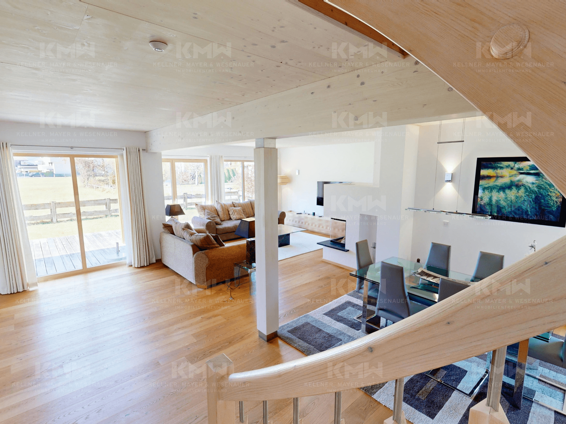 Blick von der Treppe auf den offenen Wohn- und Essbereich mit Kamin und Holzboden.