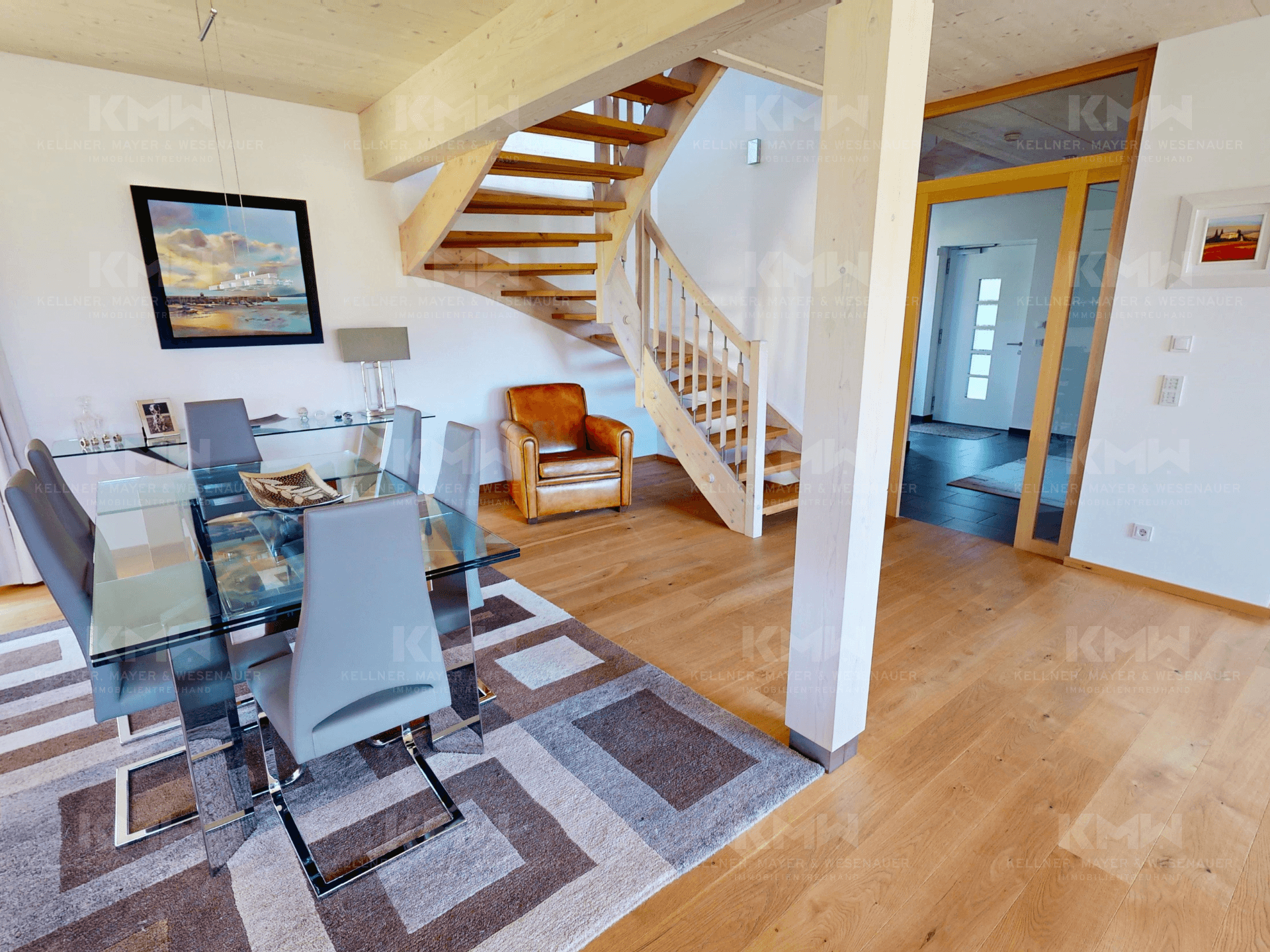 Essbereich mit elegantem Glastisch, Holztreppe und Parkettboden, offen zum Wohnbereich.