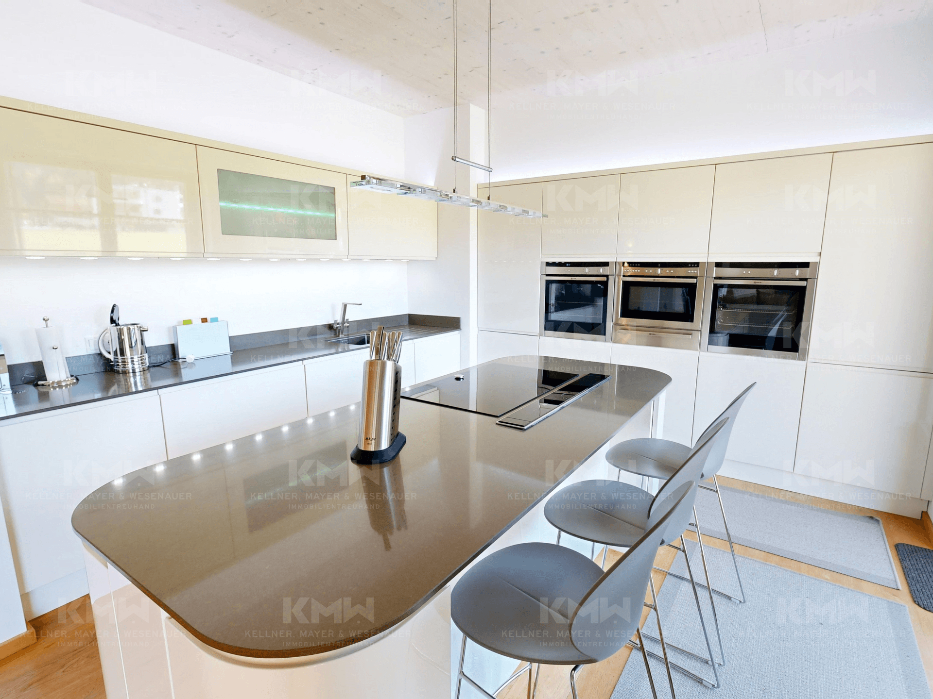 Elegante weiße Küche mit Kücheninsel, Induktionskochfeld und hochwertigen Einbaugeräten.