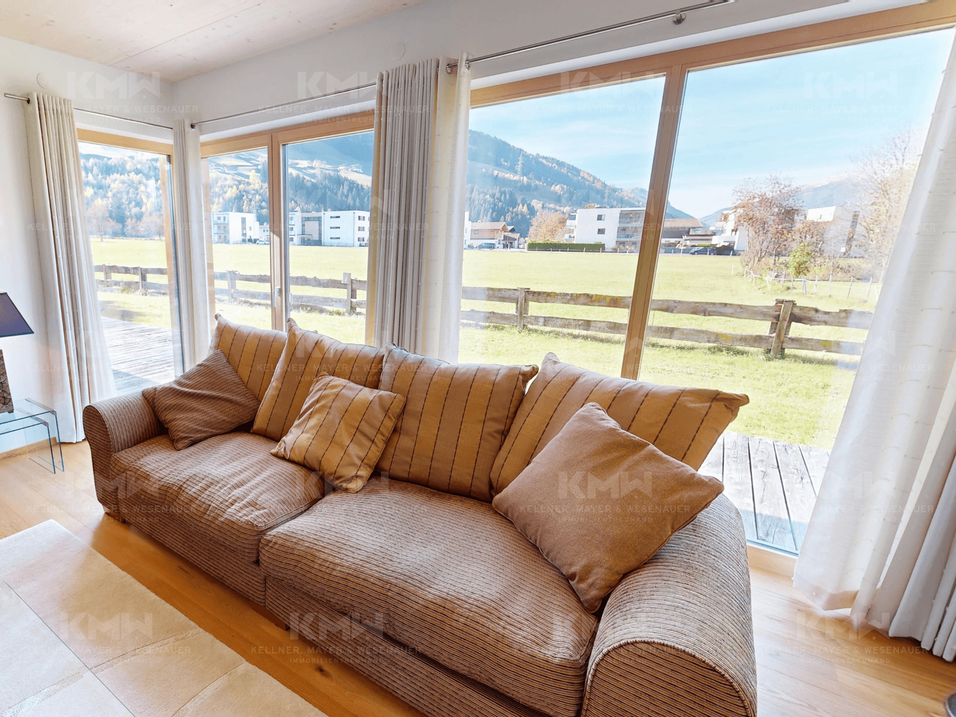 Gemütliches Sofa im Wohnzimmer mit großen Fenstern, die viel Tageslicht und Ausblick bieten.