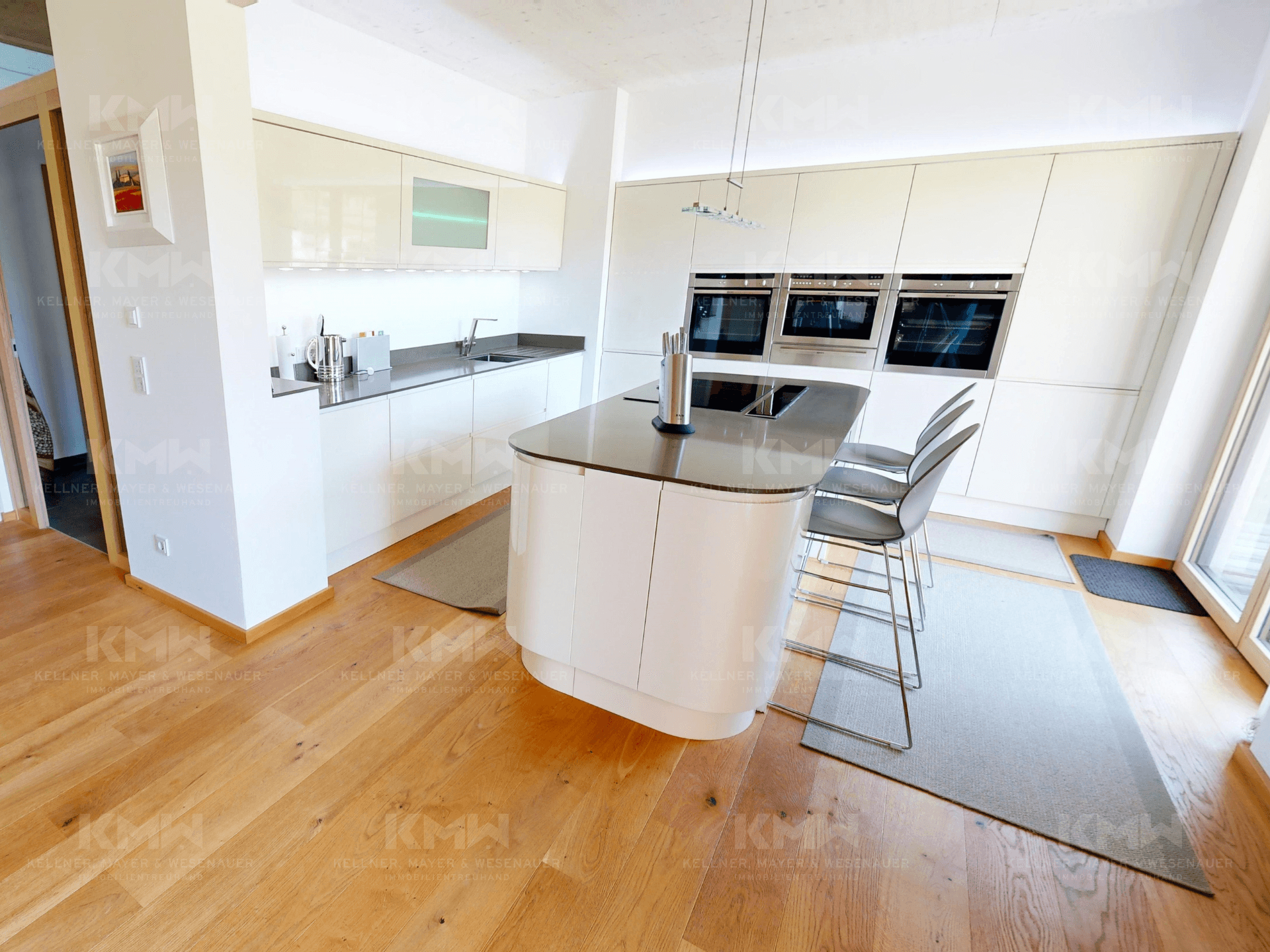 Moderne weiße Küche mit Hochglanzfronten, Kücheninsel und integrierten Backöfen.