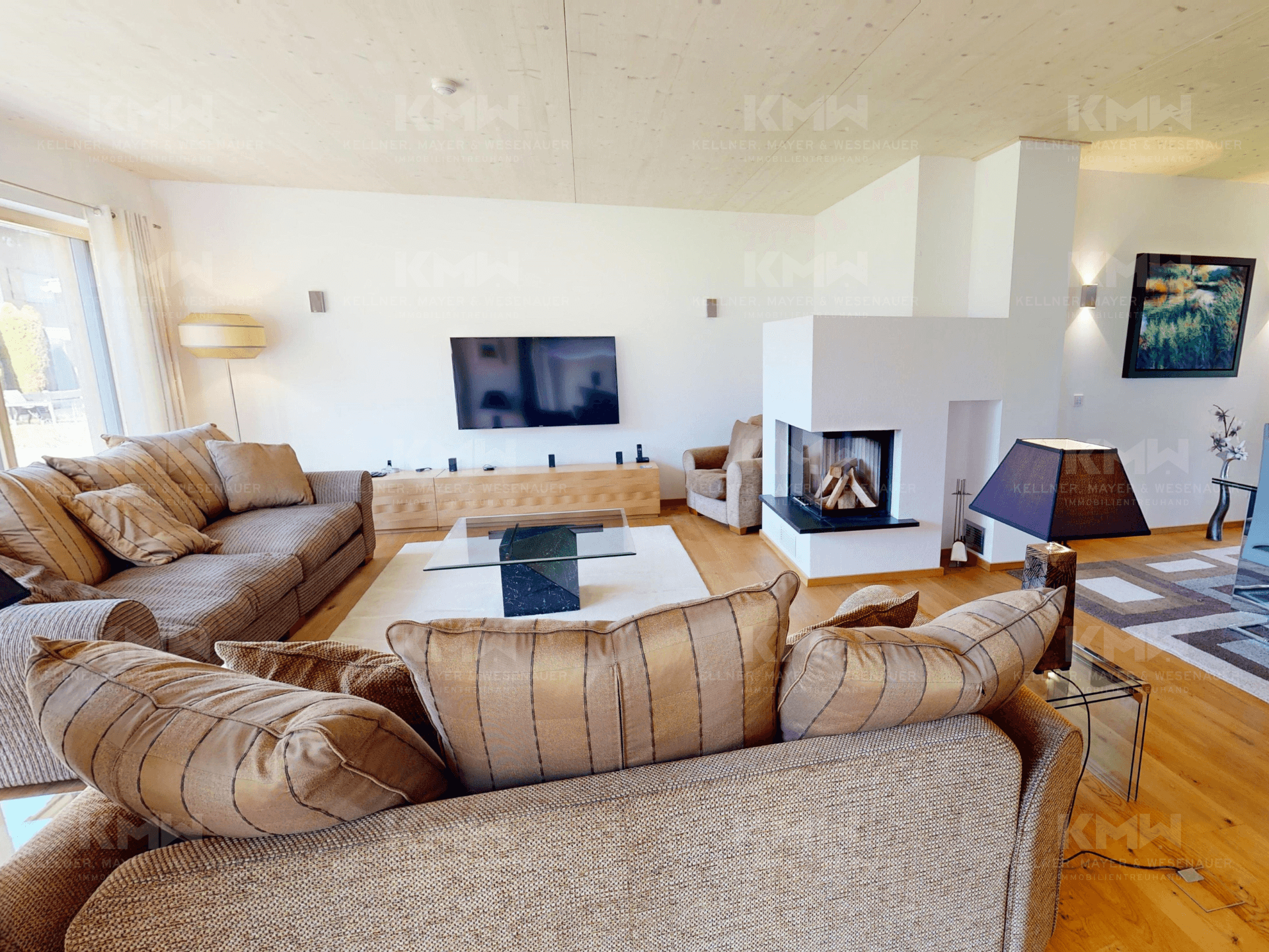 Modern eingerichtetes Wohnzimmer mit großem Fernseher, Kamin und viel Tageslicht.