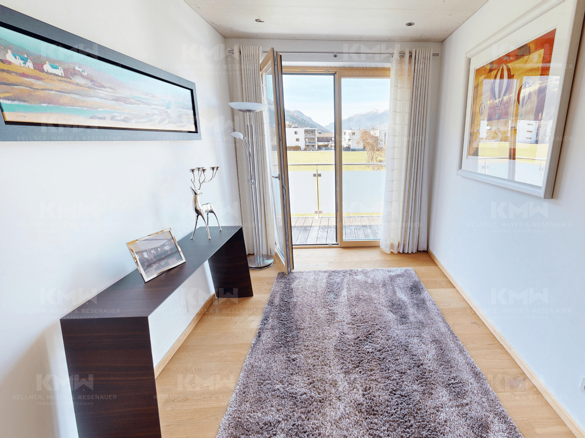 Heller Flur mit Holzboden, großen Fenstern und Zugang zu einem Balkon oder einer Terrasse.