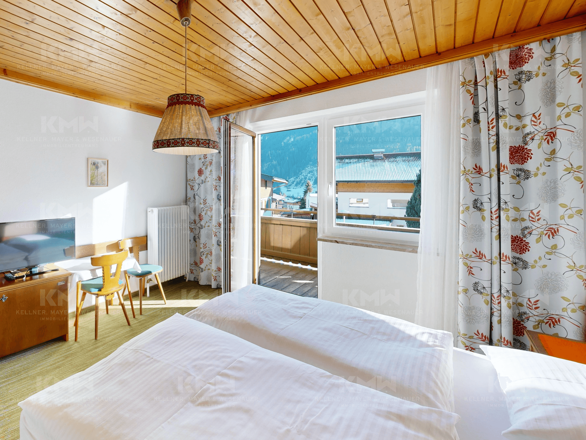 Helles Schlafzimmer mit Holzbalkendecke, Teppichboden und Balkonzugang mit Bergblick.
