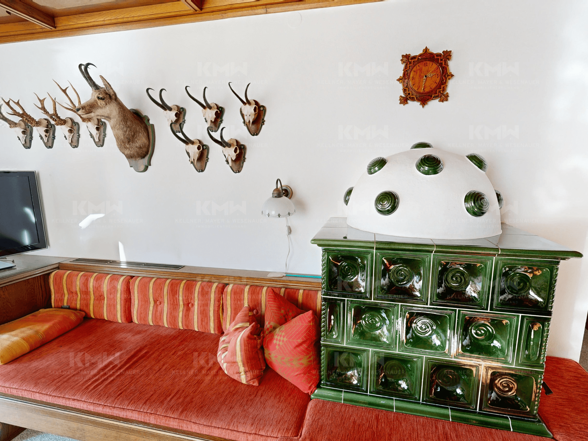 Detailansicht des traditionellen Kachelofens im Wohnbereich mit gemütlicher Sitzbank und Jagdtrophäen.