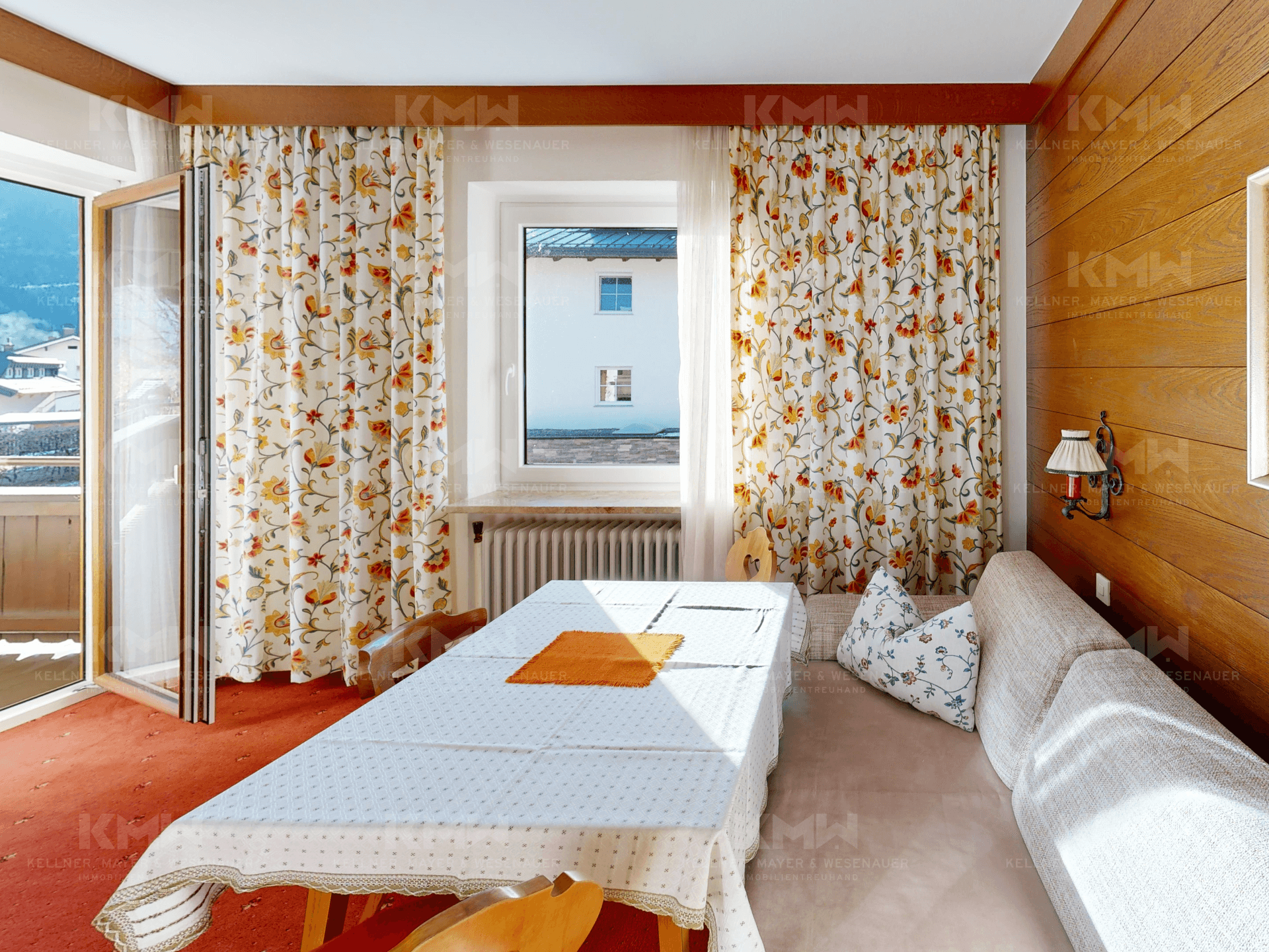 Essbereich mit traditionellen Holzmöbeln, floralen Vorhängen und Zugang zum Balkon.