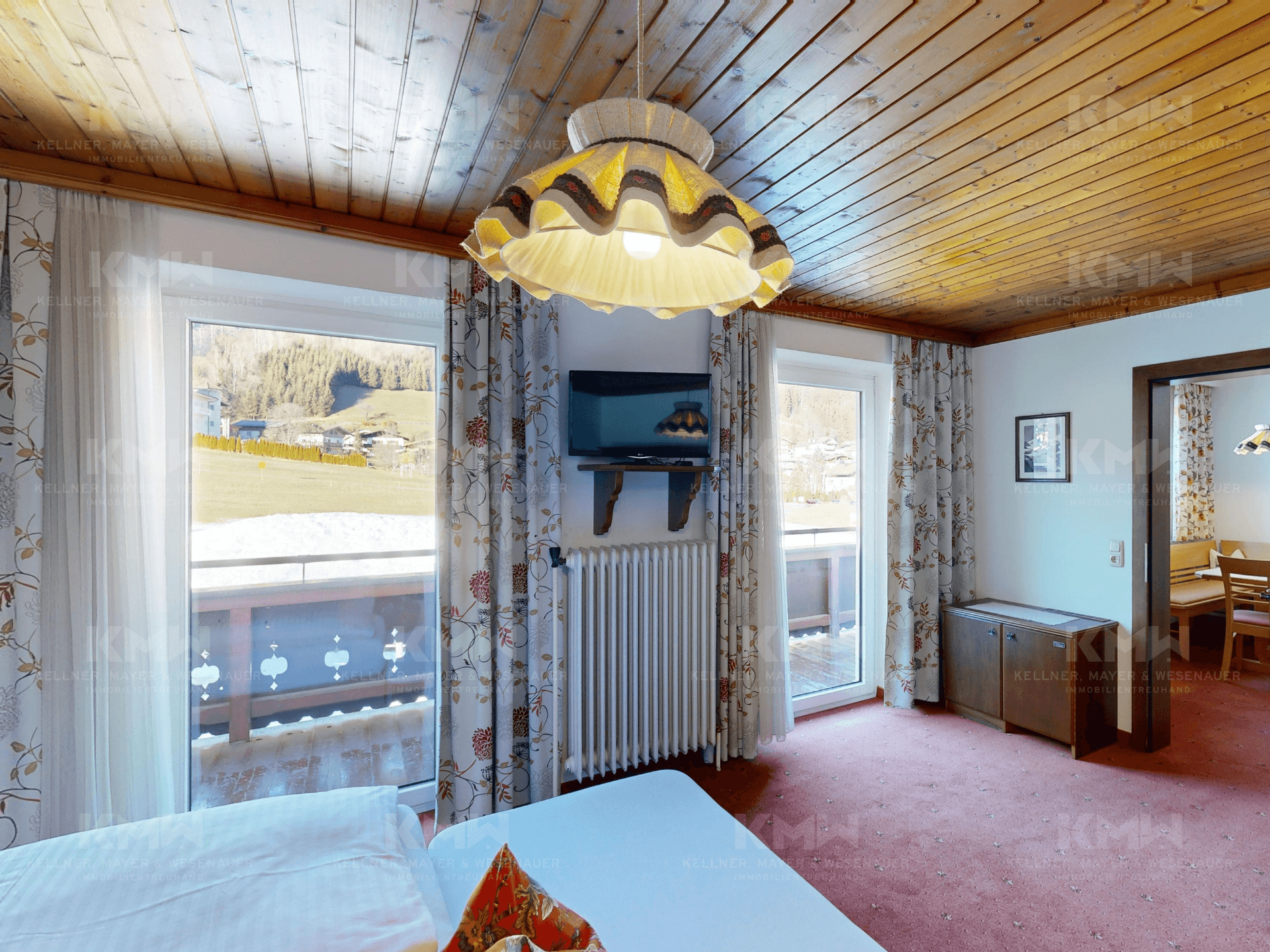 Schlafzimmer mit Holzbalkendecke, Teppichboden und Balkonzugang mit Blick auf die Berge.