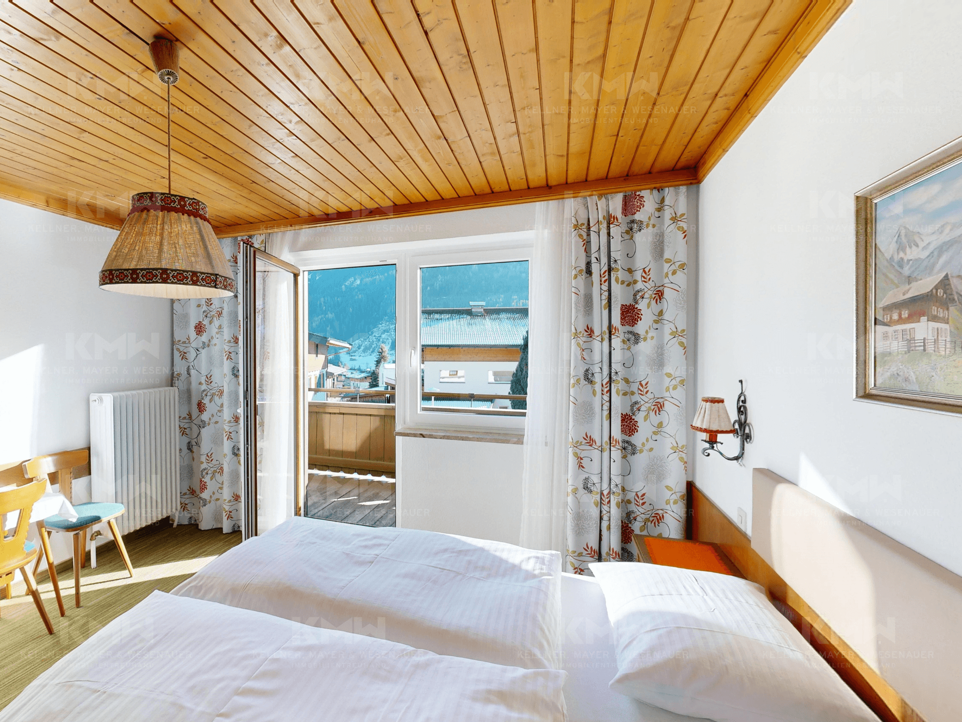 Helles Schlafzimmer mit Holzbalkendecke, Teppichboden und Balkonzugang mit Bergblick.
