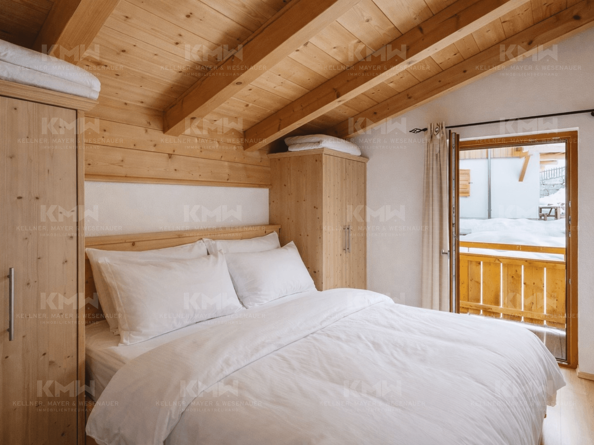 Gemütliches Schlafzimmer mit Holzbalkendecke, Holzwänden und Zugang zu einem kleinen Balkon.