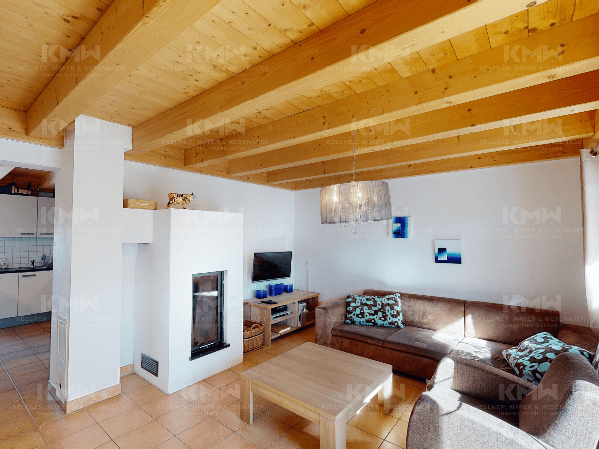 Geräumiges Wohnzimmer mit Kamin, Holzbalkendecke und offenem Übergang zur Küche.